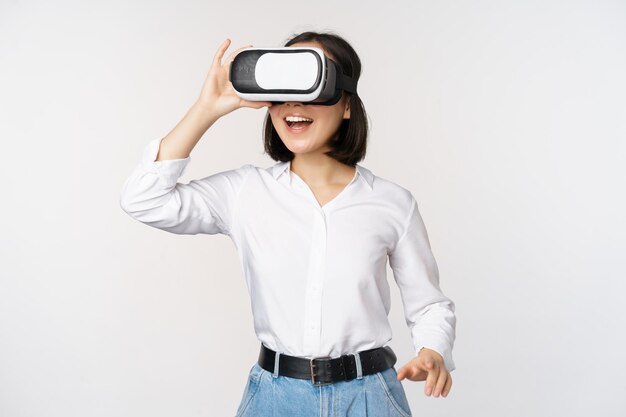 Free Photo excited young woman enter virtual reality in her glasses asian girl using vr headset standing over white background