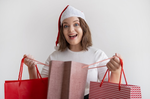 Excited young woman opening shopping bag and looking at camera