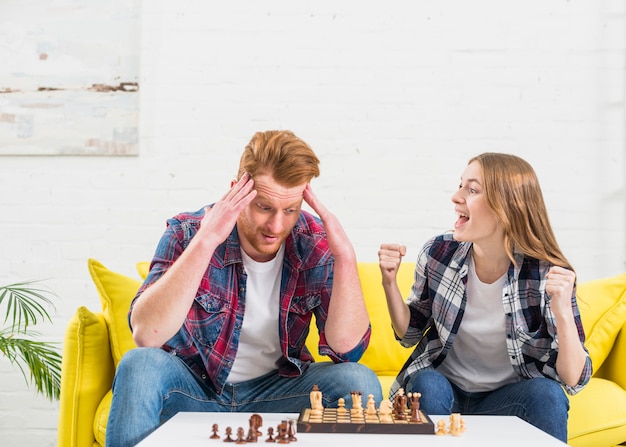 Free photo excited young woman sitting with her boyfriend cheering after winning the chess game