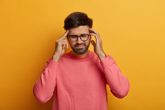 Free photo exhausted bearded man suffers from unbearable headache