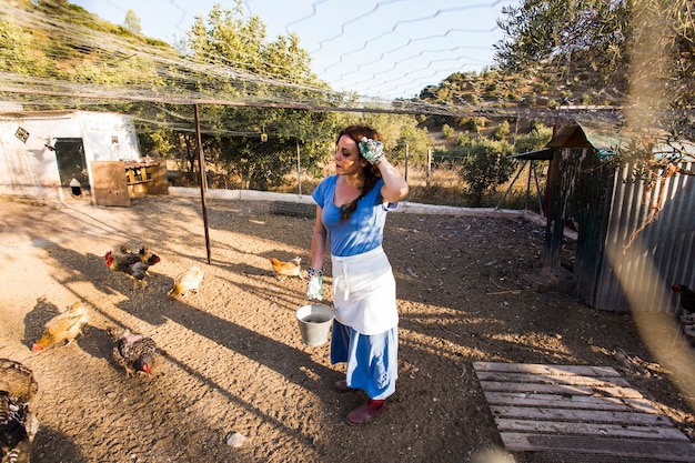 Free Photo exhausted female farmer feeding chicken in the field