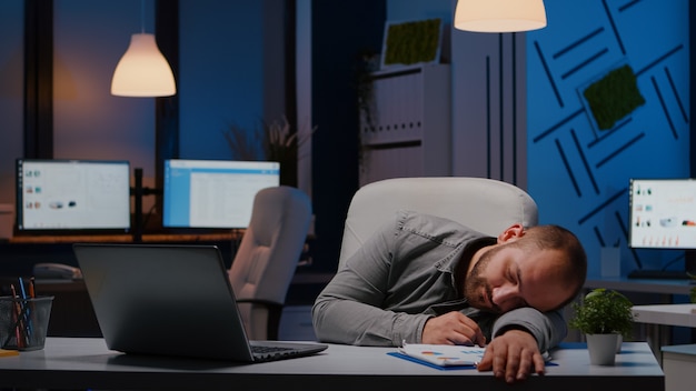 Free photo exhausted overworked businessman sleeping on desk table in startup business office