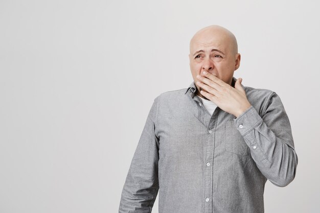 Exhausted sleepy bald adult man yawning, cover face and look left