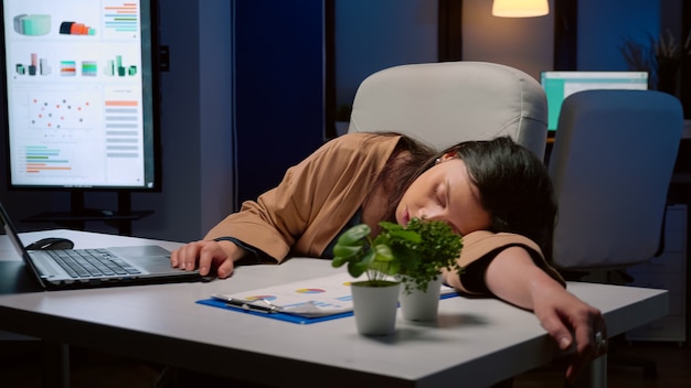 Free photo exhausted tired businesswoman sleeping on desk table in startup business office