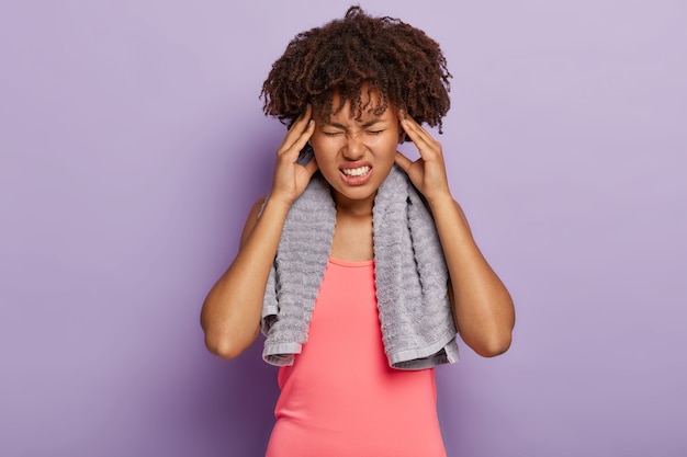 Free photo exhausted tired dark skinned woman wears pink tanktop, touches temples