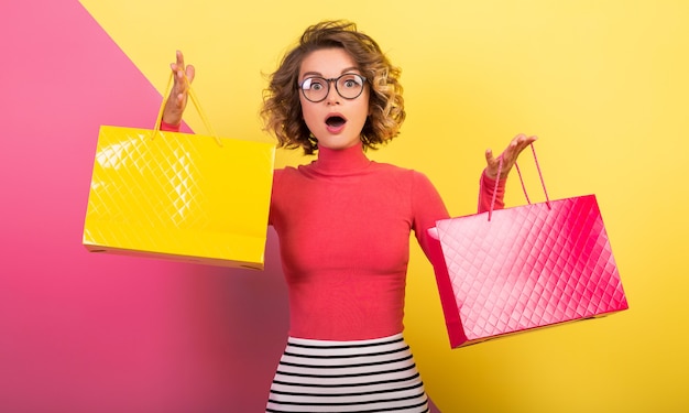 Free Photo exited attractive woman in stylish colorful outfit holding shopping bags with surprised face expression, funny emotion, pink yellow background, polo neck, striped mini skirt, sale, discout, shopaholic