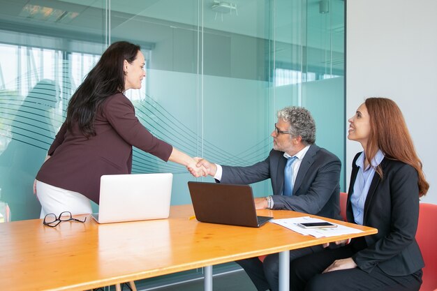 Experienced grey-haired CEO sitting and greeting businesswoman