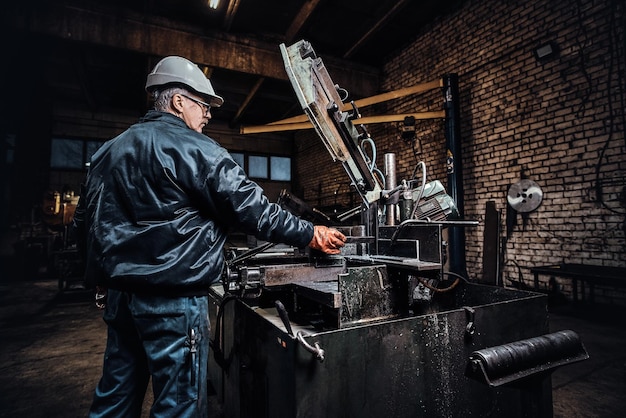 Experienced worker is working at metal factory using special machine tool.