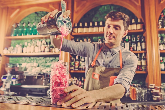 Expert barman is making cocktail at night club.