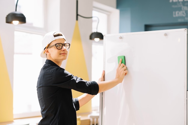 Free photo expressive schoolboy cleaning blackboard