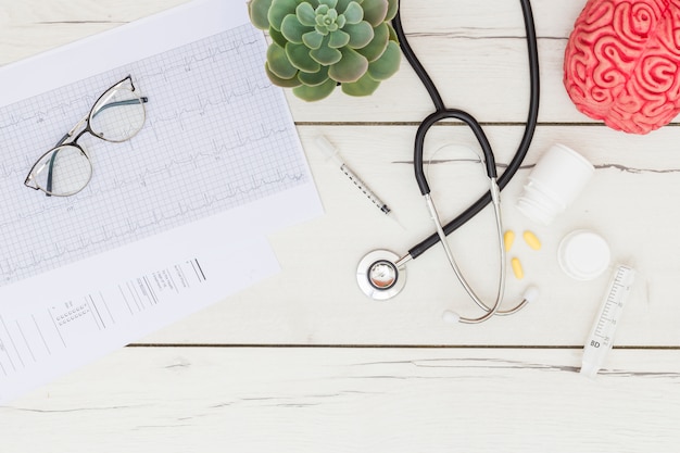 Eyeglasses on electrocardiogram; cactus plant; stethoscope; pills; syringe on desk