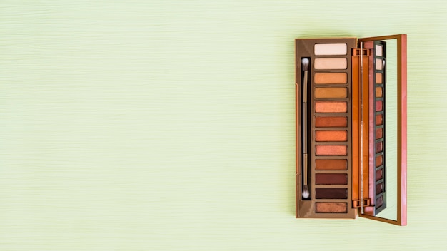 Free photo eyeshadow wooden palette with mirror and makeup brush on mint green backdrop