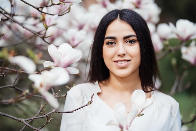 Free photo face portrait of beautiful caucasian brunette girl near blossom magnolia tree outdoors in spring park.