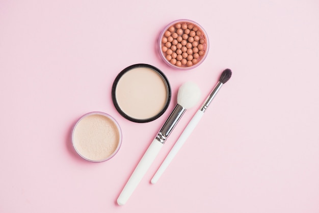 Face powders; bronzing pearls and makeup brushes on pink surface