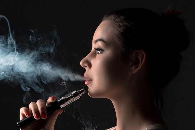 The face of vaping young woman at black studio