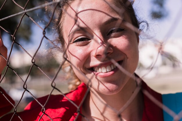 Face of young smiling girl standing behind grid