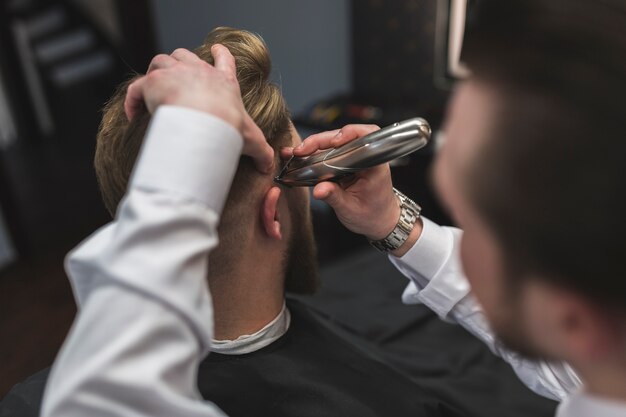 Faceless barber shaving hair of client with trimmer