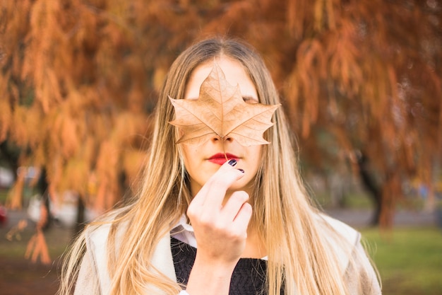 Faceless blond woman holding leaf upon face