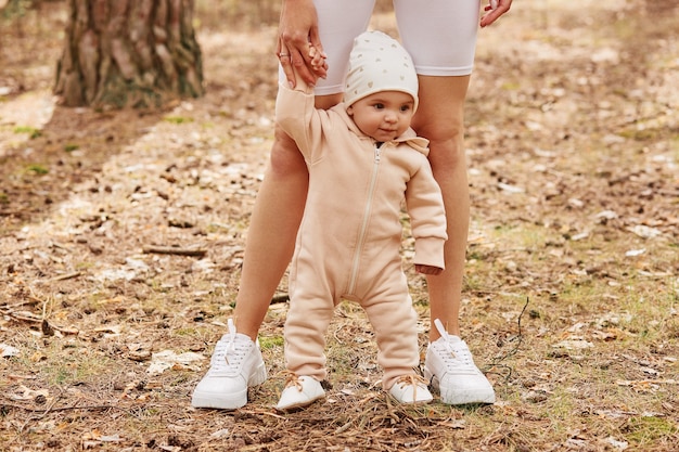 Free photo faceless female holding infant daughter hand while baby learning to go, family playing in forest