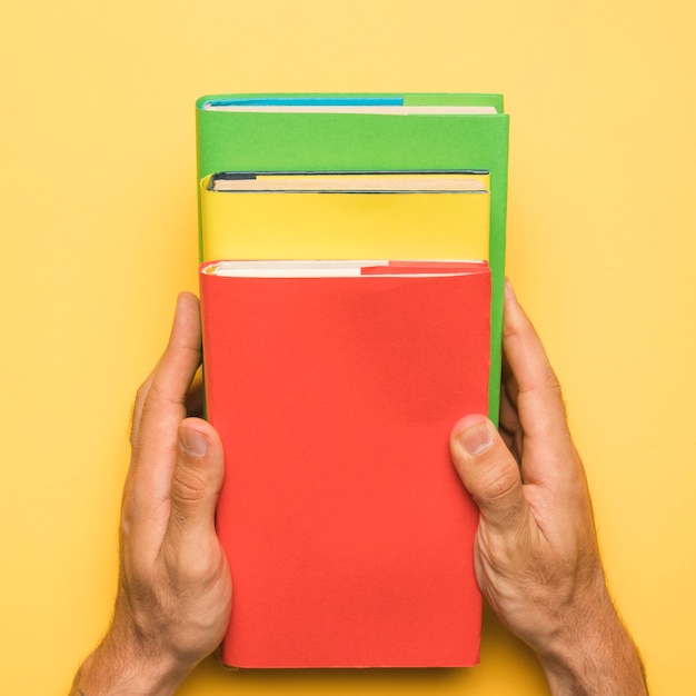 Free photo faceless person holding colorful  books on yellow background