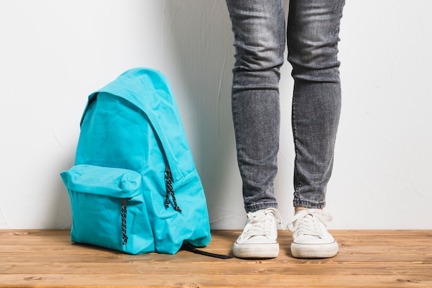 Free Photo faceless person standing beside of schoolbag on wooden table  