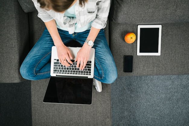 Faceless woman browsing laptop on couch