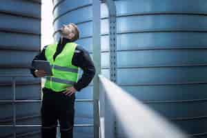 Free photo factory worker standing on metal platform between industrial storage tanks and looking up for visual inspection of silos for food production