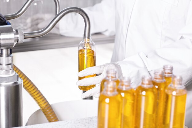 Factory worker in white gown and rubber gloves holding plastic bottle