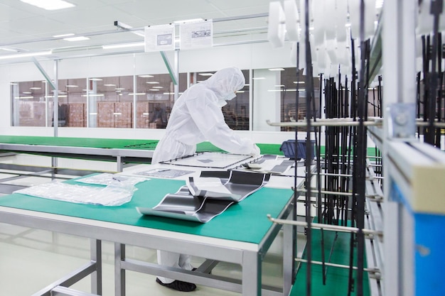 Free photo factory worker in white lab suit and face mask assembling parts of the tv set on the table