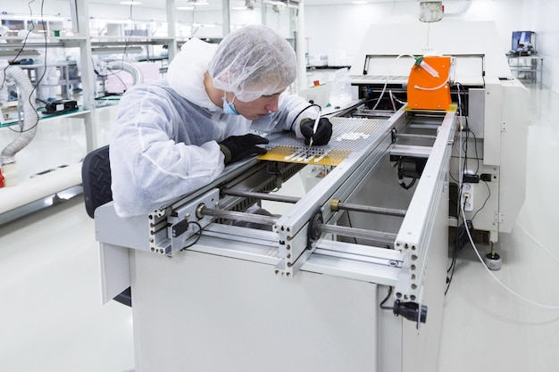 Free Photo a factory worker in a white lab suit and latex gloves working with a soldering iron and some modern equioment