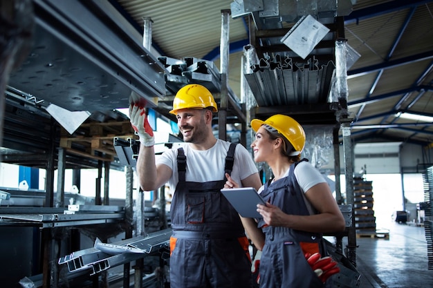 Free photo factory workers checking inventory with tablet computer in industrial warehouse full of metal parts