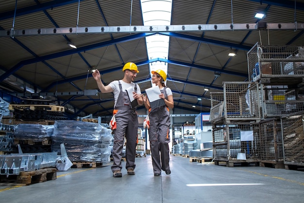 Factory workers walking through large production hall and having conversation