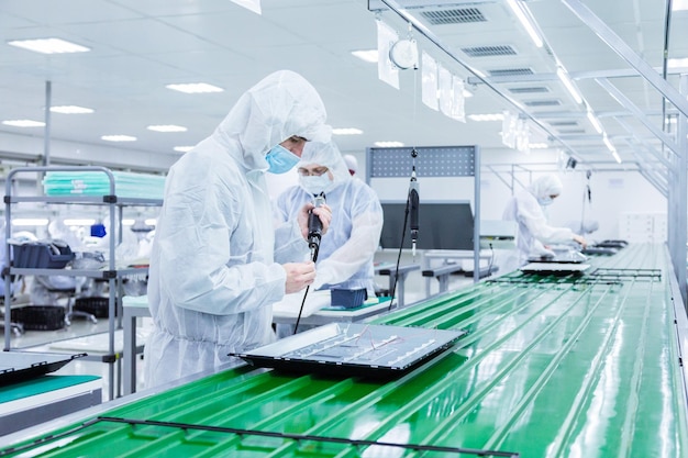 Free photo factory workers in white lab suits and face masks producing tv sets on a green assembly line with some modern equipment