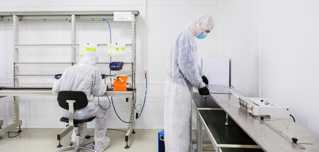 Factory workers in white lab suits and face masks producing tv sets with some modern equipment