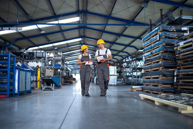 Free Photo factory workers in work wear and yellow helmets walking through industrial production hall and discussing about delivery deadline