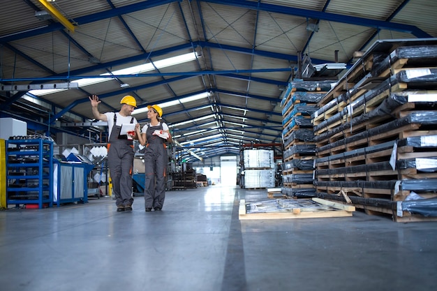 Free Photo factory workers in work wear and yellow helmets walking through industrial production hall and sharing ideas about organization