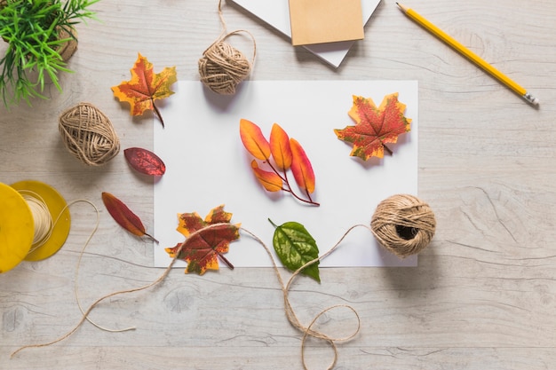 Free Photo fake autumn leaves with string spool on wooden textured background