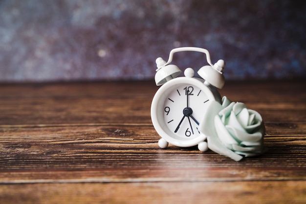 Free photo fake white rose with alarm clock on wooden background