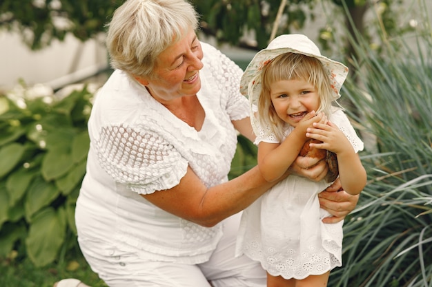 Family in a back yeard. Granddaughter with grandmother. People with little chicken.