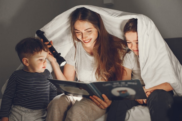 Family under the blanket in bed reading a book.