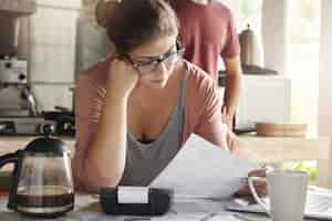 Free photo family budget and finances. serious woman doing accounts and feeling frustrated with amount of monthly expenses. young female wearing glasses calculating utility bills, sitting at kitchen table