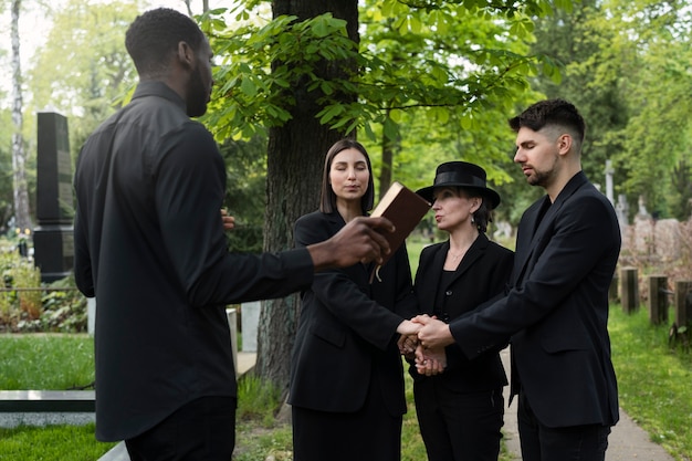 Free photo family at the cemetery holding hands while the priest reads from the bible