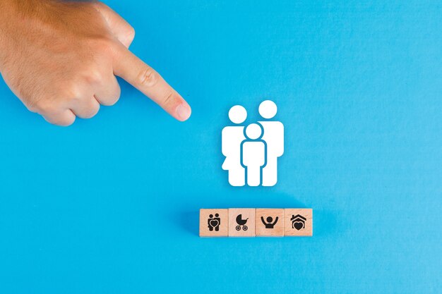 Family concept with wooden block, paper family icon on blue table flat lay. man hand pointing.