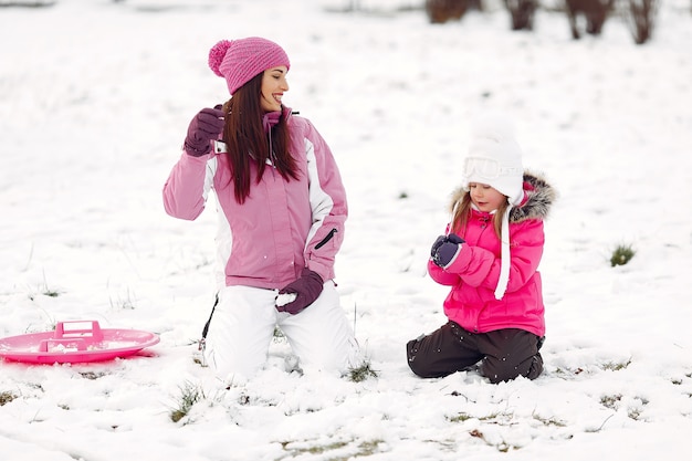 Family in knitted winter hats on family Christmas vacation. Woman and little girl in a park. People playing.