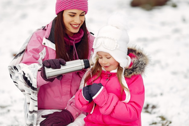 Family in knitted winter hats on family Christmas vacation. Woman and little girl in a park. People wit thermos.