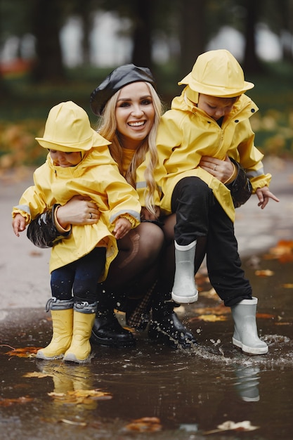 Family in a rainy park. Kids in a raincoats. Mother with child. Woman in a black coat.