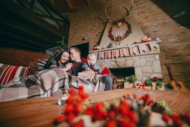 Family sitting on the couch clothed with a blanket and seen from the christmas decorations of the wooden table