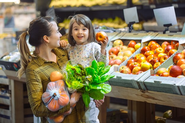 Family in the supermarket. Beautiful young mom and her little daughter smiling and buying food. The concept of healthy eating. Harvest