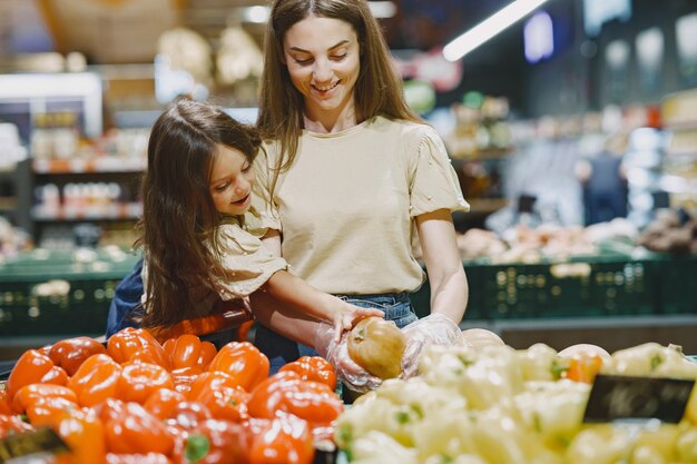 Family at the supermarket. Woman in a brown t-shirt. People choose vegetables. Mother with daughter.