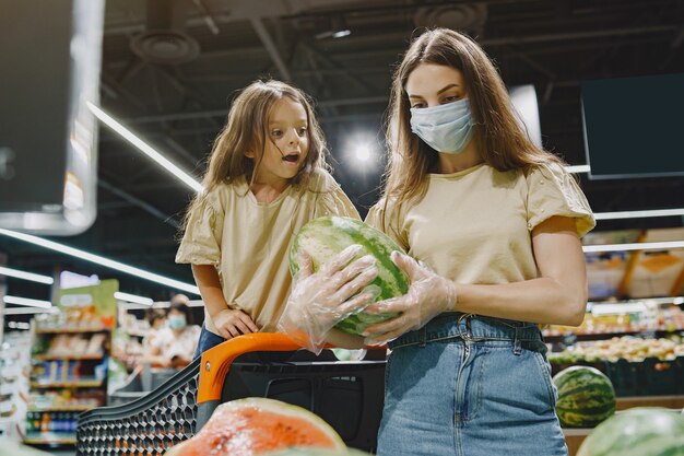 Family at the supermarket. Woman in a protective mask. People choose vegetables. Mother with daughter. Coronavirus.